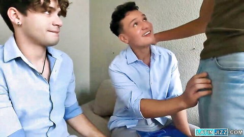 Two young smiling guys in shirts sit on couch as woman grabs his cock bulge through jeans in gay threesome tease