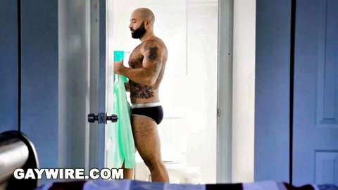 Hairy tattooed bald DILF in tight black briefs holding green towel by shower door