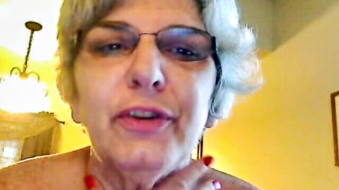 Mature webcam babe with gray curly hair, glasses, and red accents teasing curves