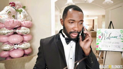 Black groom in tuxedo on phone at wedding, pre-gangbang frenzy with brides