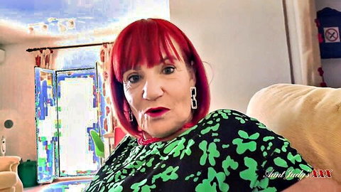 Mature redhead GILF in sexy green top sitting on couch with pursed lips
