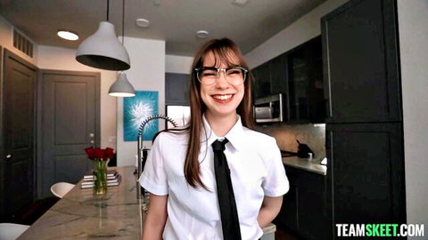Cute brunette in glasses and schoolgirl shirt tie smiling teasingly in kitchen