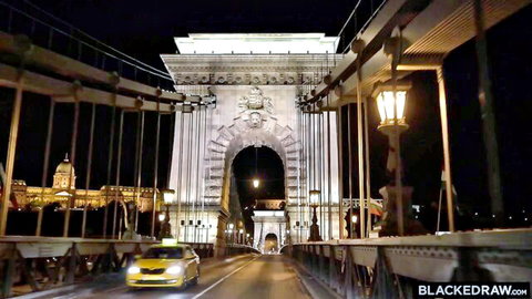 Night view of Budapest Chain Bridge lit up with yellow taxi driving and Parliament building in background