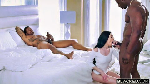 Brunette in white dress kneels sucking massive BBC while tattooed black stud watches naked on bed