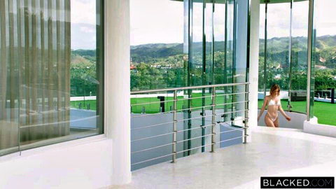 Petite blonde in tiny white bikini struts seductively on luxury balcony with hill views