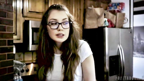 Young brunette teen with glasses smiles seductively in kitchen wearing tight white top