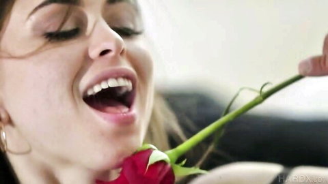 Riley Reid close-up smiling with red rose stem in open mouth, teasing expression