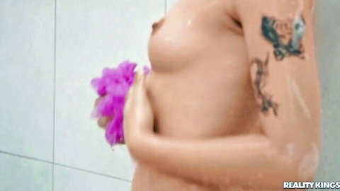 Tattooed short-haired woman nude in shower with purple loofah