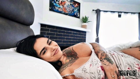 Izzy Star in lacy lingerie, smiling with big tits and tattoos on bed