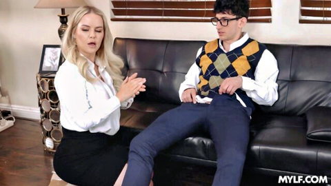 Blonde MILF in blouse and skirt kneels before young glasses-wearing stud on couch in taboo tease