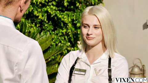 Blonde hotel receptionist in uniform smiling at suited guest outdoors