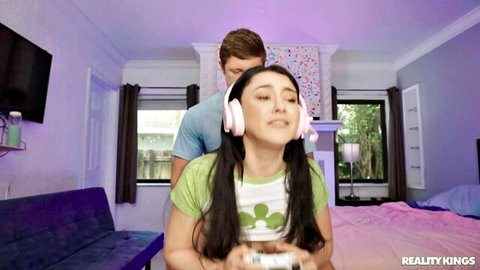 Cute gamer girl with pink headphones plays Xbox controller while guy fondles her from behind