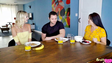 Blonde stepsister in yellow top and brunette friend in floral dress eat breakfast teasing stepbrother at table