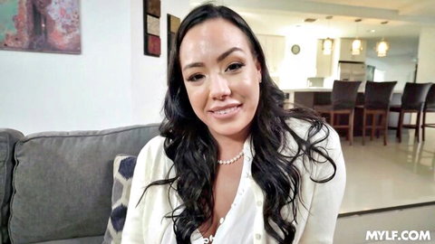 Smiling Asian MILF teases deep cleavage in unbuttoned white blouse on couch