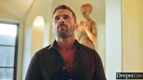 Handsome bearded man in unbuttoned black shirt gazes intensely with golden statue in luxurious room