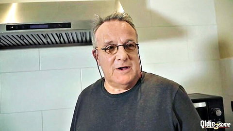 Older man with glasses and gray hair speaking in kitchen with Qlide3some watermark