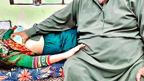 South Asian husband gropes wife's thigh on bed wearing colorful shalwar kameez