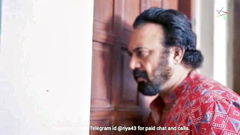 Bearded Asian man in red kurta with ponytail, intense gaze