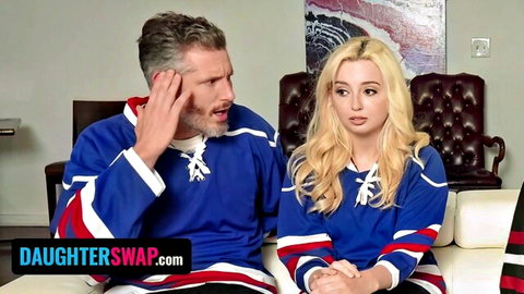 Surprised muscular stepdad in blue hockey jersey sits with busty blonde stepdaughter in matching jersey on couch