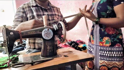 South Indian tailor measuring curvy woman in floral dress at vintage sewing machine