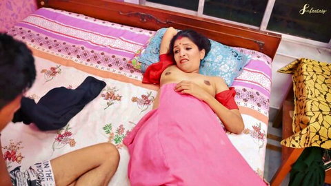 Topless South Asian MILF with big tits lies on bed as man fucks her missionary style saree pulled up