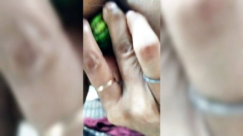Blurry close-up of dark-skinned hands with rings holding green fruit near blurred mouth