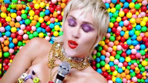 Miley Cyrus topless exposing perky tits lying in colorful candy balls gripping microphone seductively