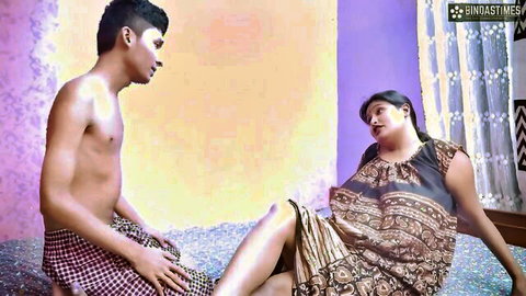 Shirtless young Indian man stares at busty BBW mature woman lounging with legs spread in colorful saree