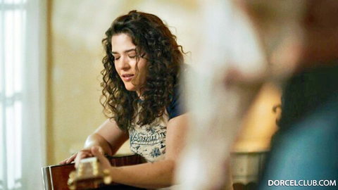 Curly haired brunette in tight top strums guitar seductively with man watching