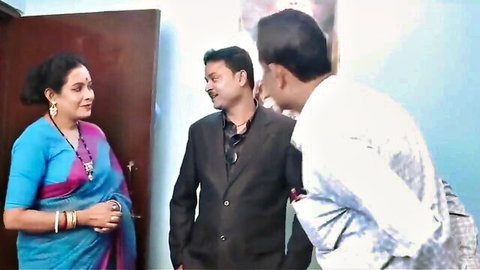Mature Indian woman in blue saree chats with two suited men near wooden door