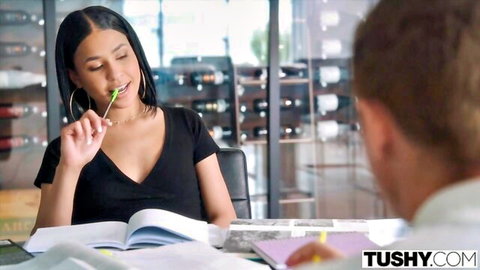 Young brunette with big tits teases by sucking green pen on lips showing deep cleavage at desk