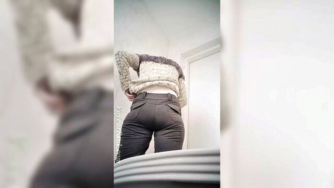 Pale mature woman pulls down gray pants exposing big white ass cheeks in bathroom.