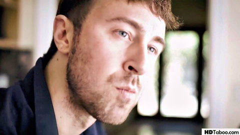Close-up of rugged Caucasian man with stubble, blue eyes, and intense gaze in taboo scene