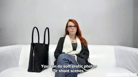 Redhead with glasses sits clothed on casting couch for soft erotic photos