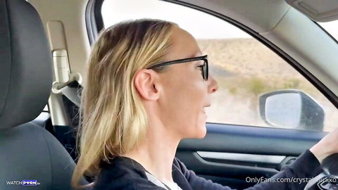 Blonde MILF in glasses smiles while driving car in desert showing profile view