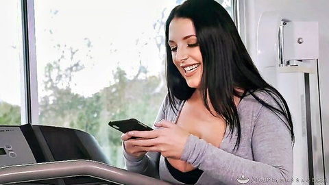 Angela White smiles on treadmill after workout, cleavage in grey sweater