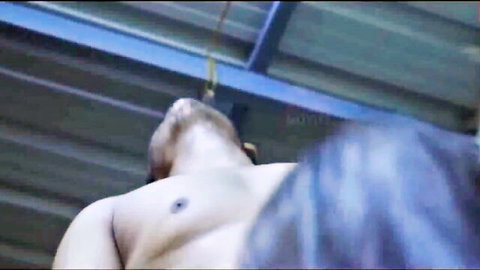 Muscular shirtless man suspended by rope in intense BDSM scene with dark-haired woman