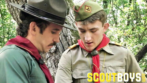 Scoutmaster and young scout in uniforms gaze intently in forest, gay roleplay tease