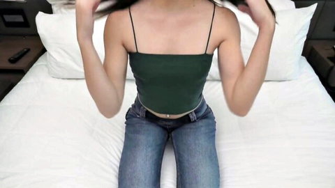Tall amateur teen in green tank top and low-rise jeans posing on bed
