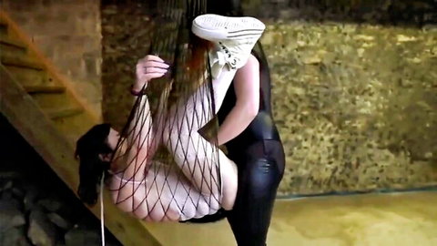 Brunette dominates suspended shemale in fishnet and leather