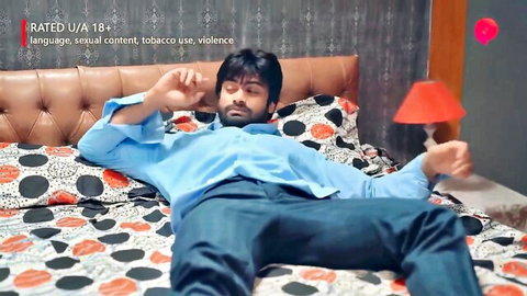 Handsome Indian man lounging on bed in blue shirt, Hindi web series scene