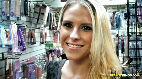 Blonde Sammie Rhodes smiling in sex shop surrounded by toys