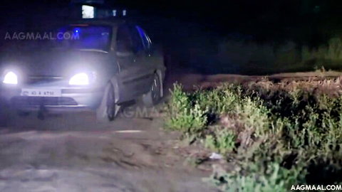 Black car parked on dirt road at night surrounded by bushes in Indian outdoor scene