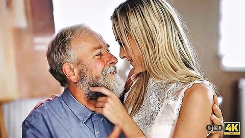 Petite young blonde smiles seductively as old bearded man embraces her waist intimately