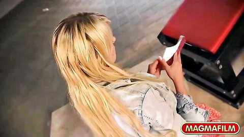 Blonde babe in denim jacket checks phone on red bench teasing viewers