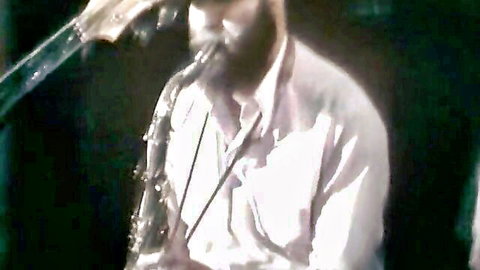 Bearded musician intensely playing saxophone in white shirt performance