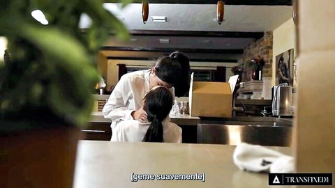 Brunette in white shirt passionately kisses ponytail Asian beauty on kitchen counter