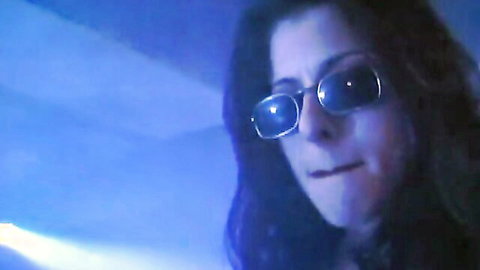 Seductive brunette with glasses smirks with parted lips in blue-lit closeup