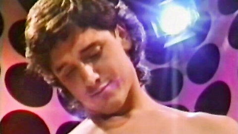Retro 80s porn thumbnail: long-haired shirtless man in spotlight, Tracey Wynn scene
