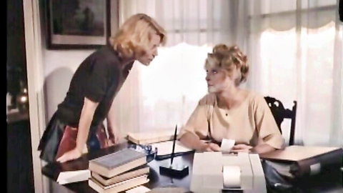 Two blondes in vintage office argue intensely over desk in naughty retro confrontation